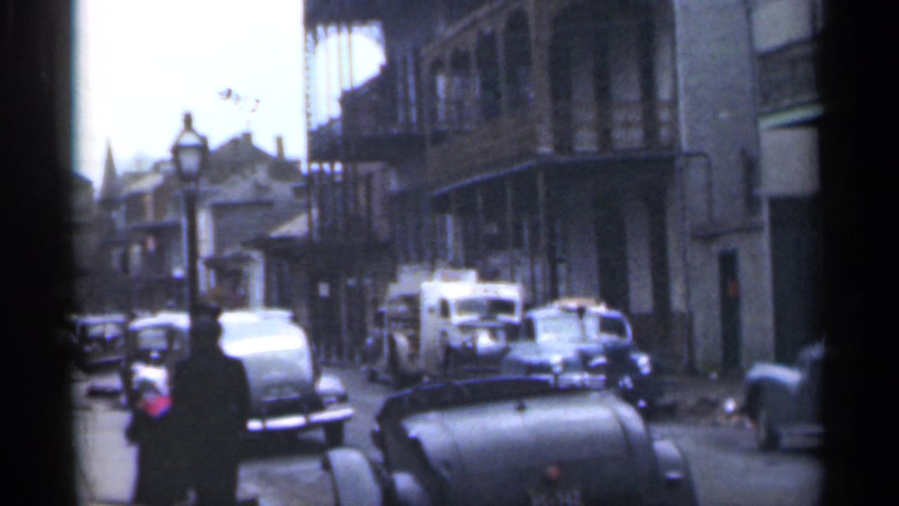 Car-lined street with a lone woman walking near a black convertible and older buildings.