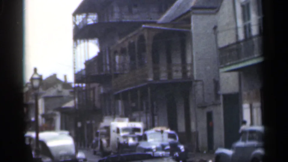 1949 Santa Cruz home-movie frame with car-lined curb, balcony structures, storefront-like facades, and a partially visible pedestrian.