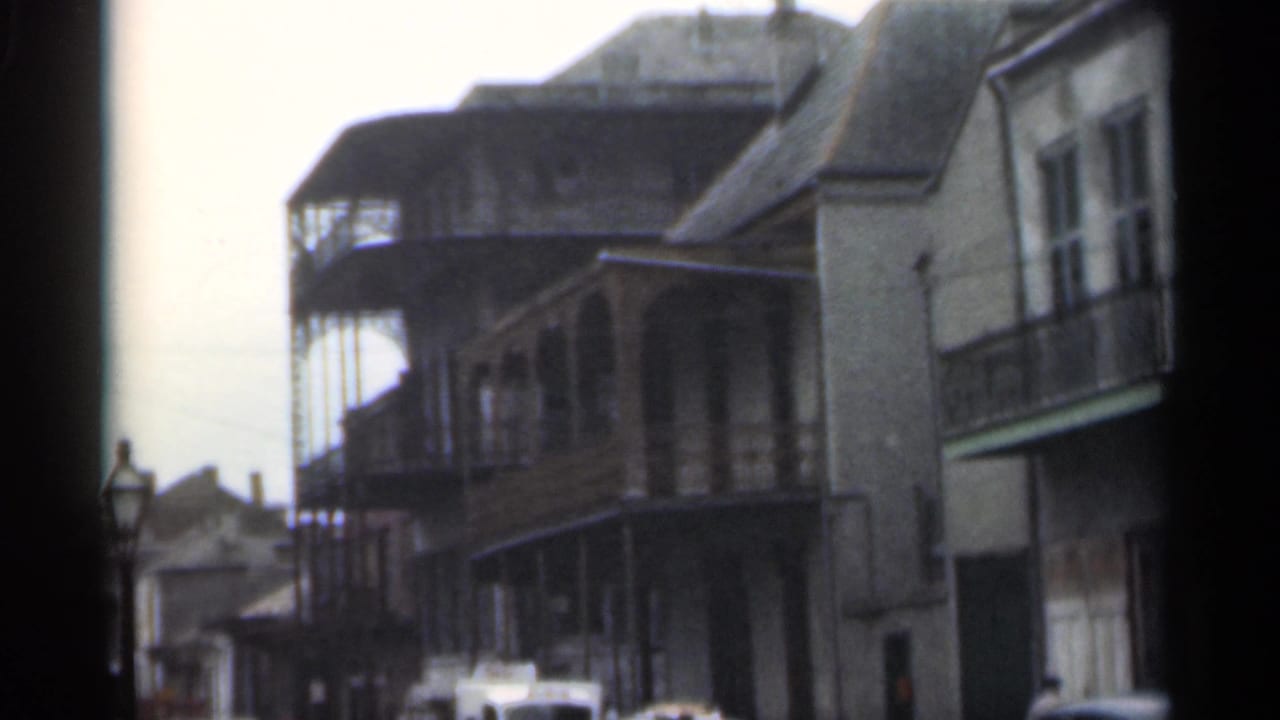 Street-facing buildings with upper balconies, a lamp post, and parked vehicles partly visible below.