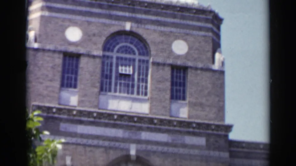 1954 New York 8mm frame showing the upper section of a stone building with an arched central window and decorative round details.