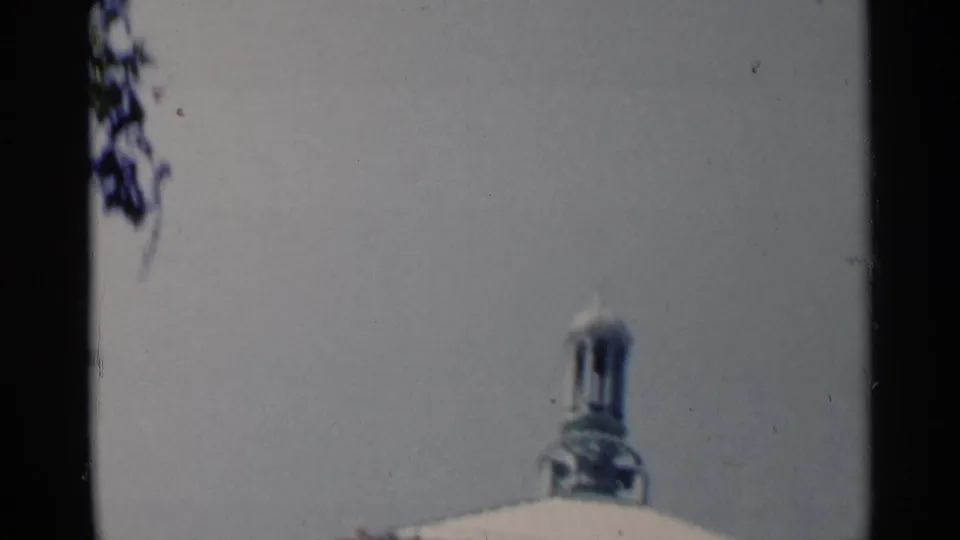 Soft 8mm frame showing a pale vertical surface and a small monument-like detail, with heavy gate edge and blur.