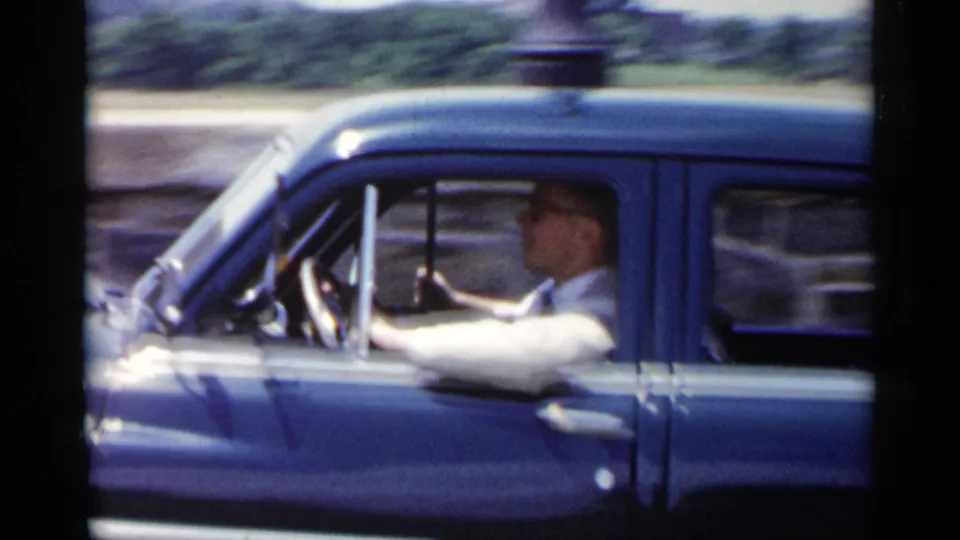1954 New York home-movie view of the blue sedan in motion, with the driver framed in profile at the wheel.