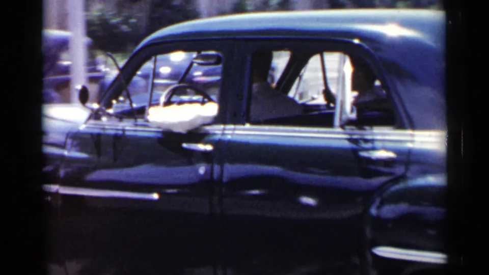 Later frame of the 1954 New York driving scene, showing the blue sedan from the side as it continues past the camera.