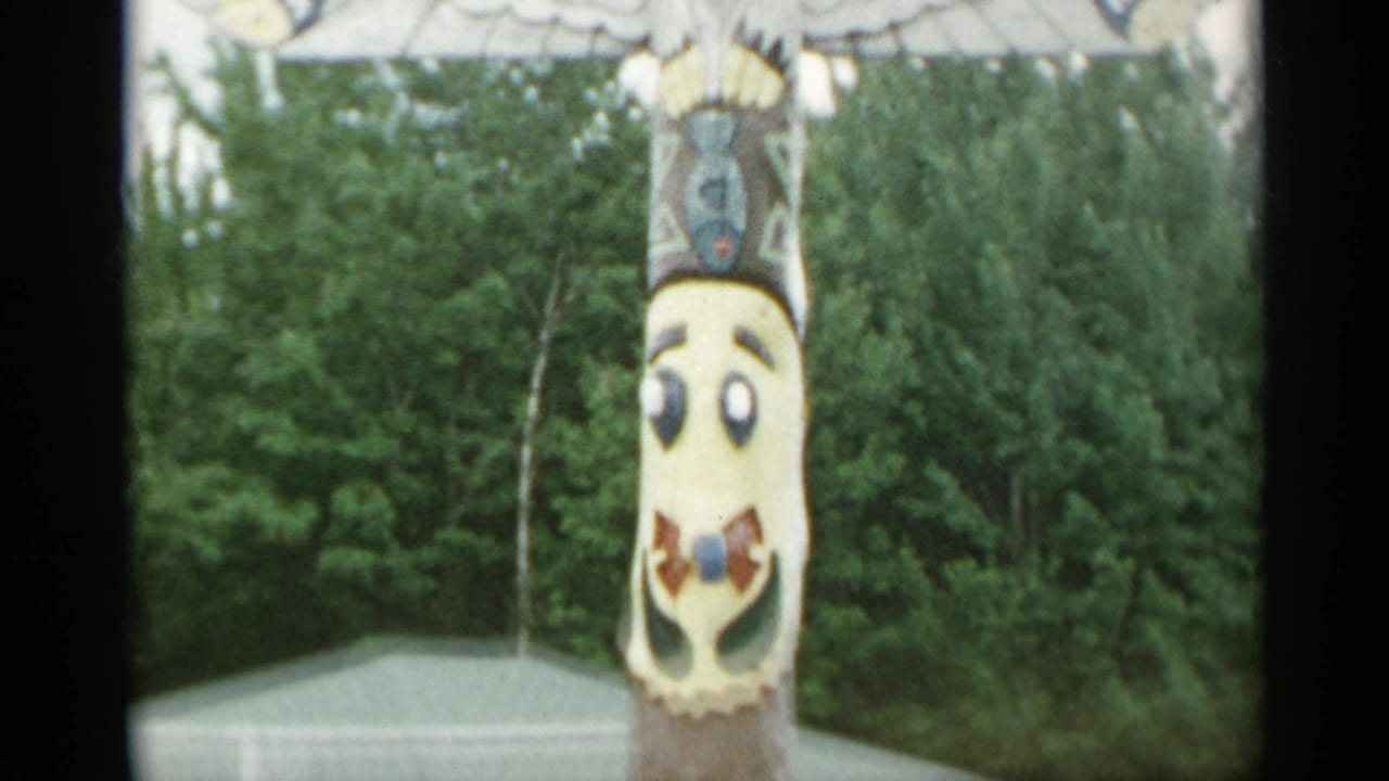 Tall painted pole in a garden setting with trees and a small roof behind it.