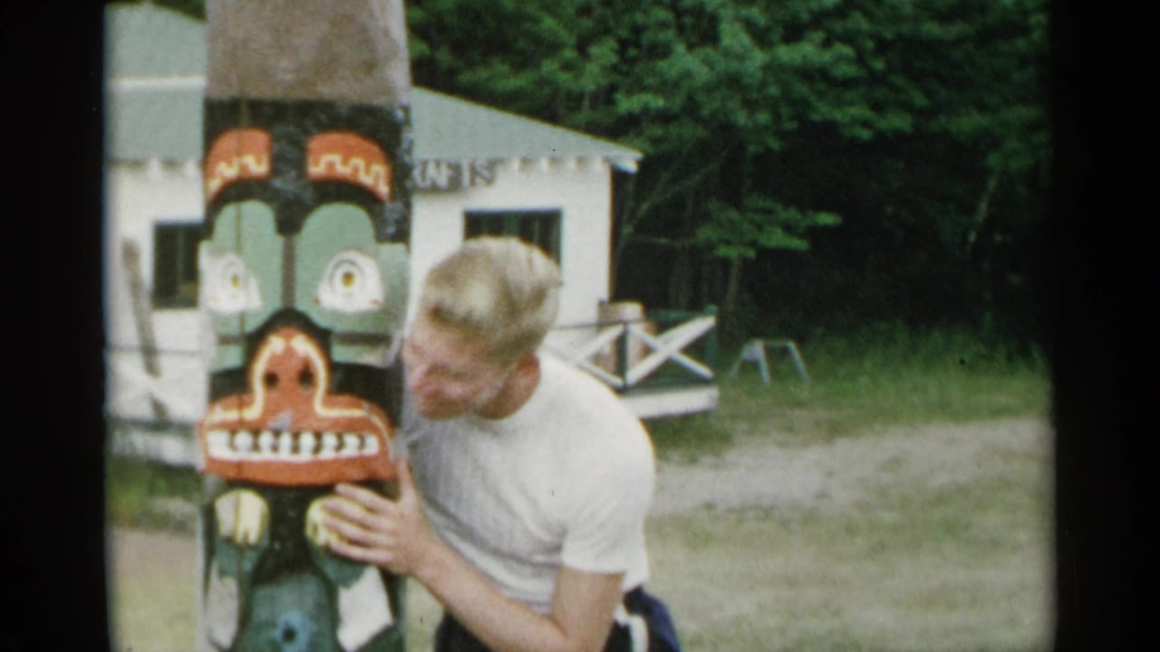 Man leans toward the painted totem pole with his hands on it.
