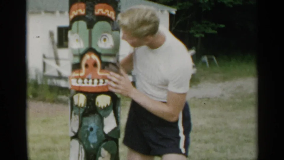 At the end of the 1954 New York clip, the man stands beside the painted totem pole and looks down toward its carved surface.
