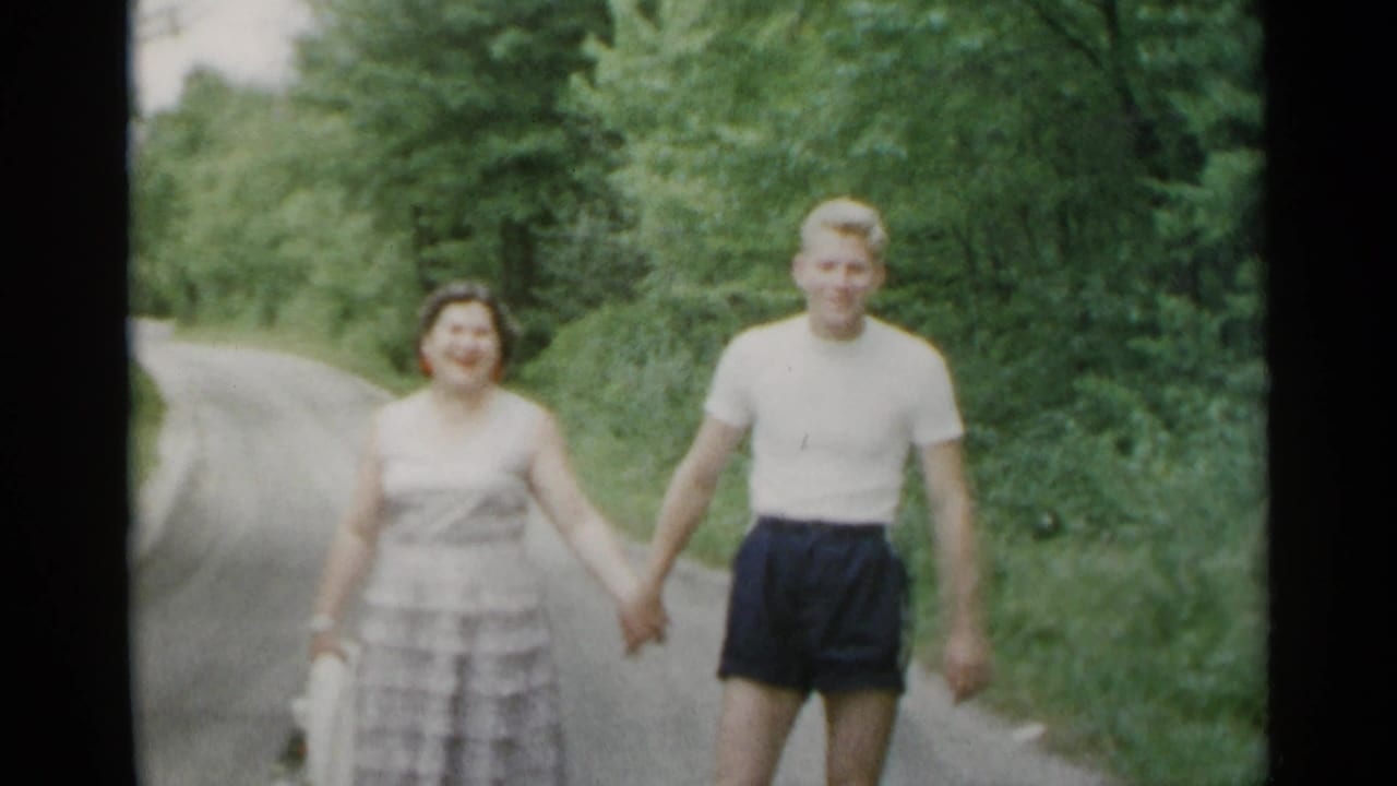 Woman and young man holding hands on a narrow road lined with trees.