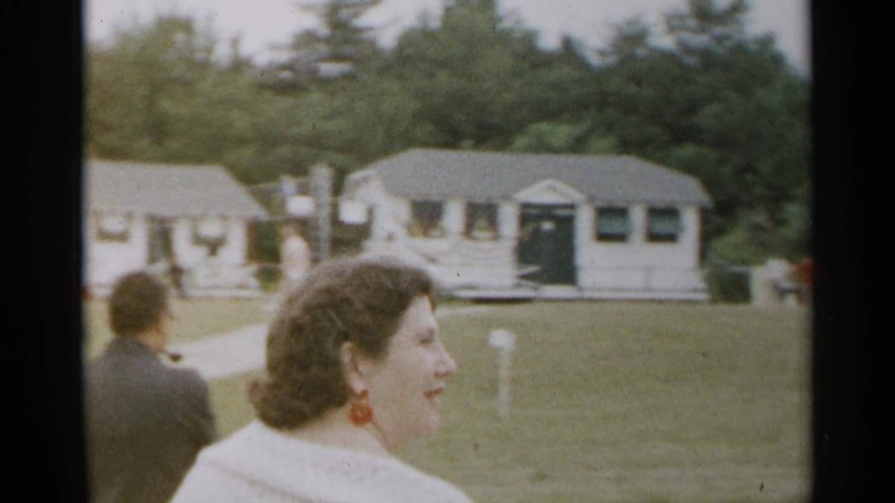 Woman in a light sweater smiles in profile near a lawn and cottages.