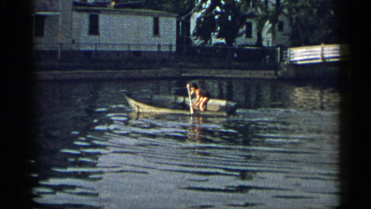 Person rowing a yellow rowboat on a calm waterway near shoreline houses.
