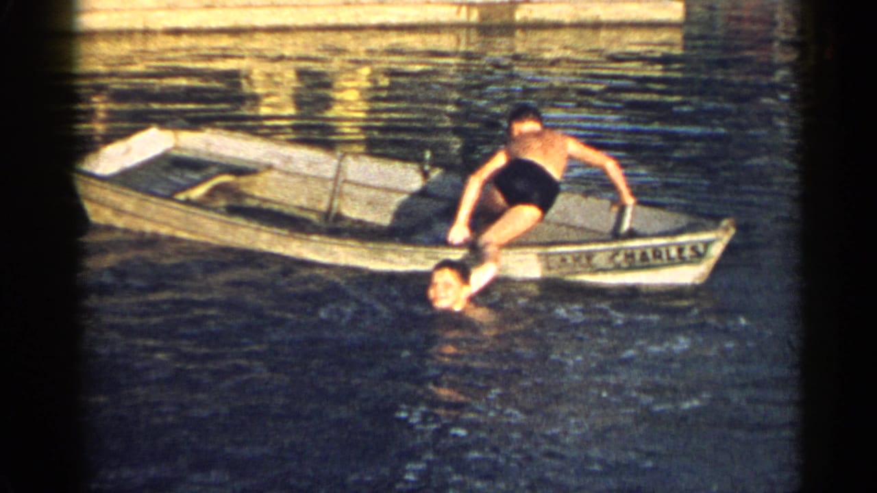 Two men in and beside a small wooden boat on a lake, one partly submerged in the water.