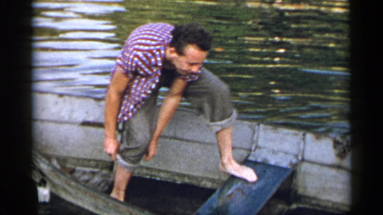 Adult man in a red striped shirt and rolled trousers steps barefoot into a small boat on a New York lake in 1954 footage.