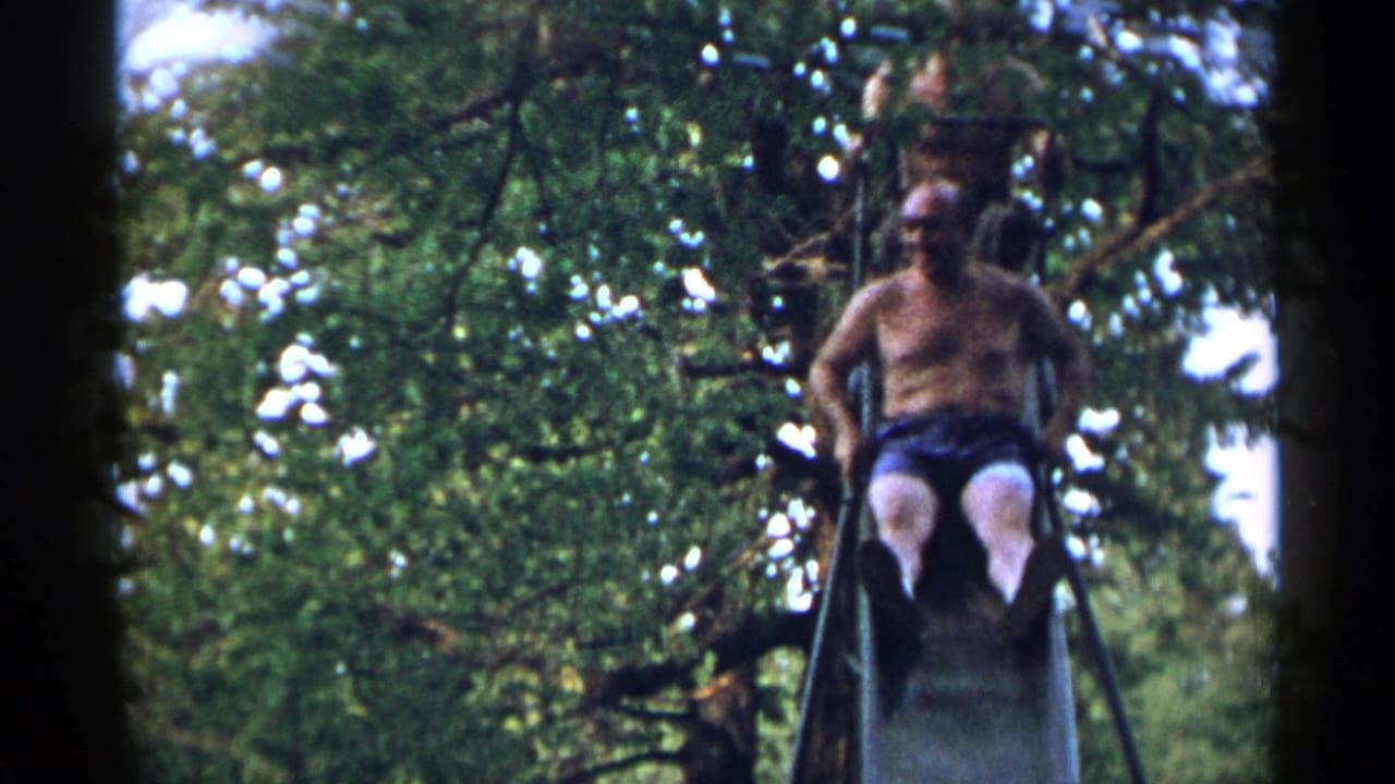 A shirtless older man rides down a metal slide while another person is partially visible above, framed by trees in 1954 New York footage.