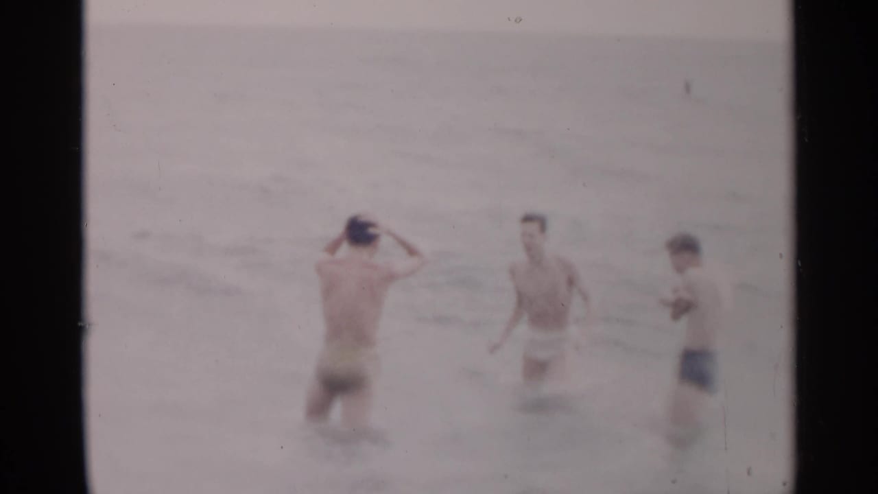 Three young men stand waist-deep in ocean water, with one adjusting a swim cap.
