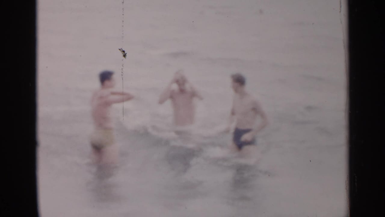 Three men splash and stand in shallow ocean water.