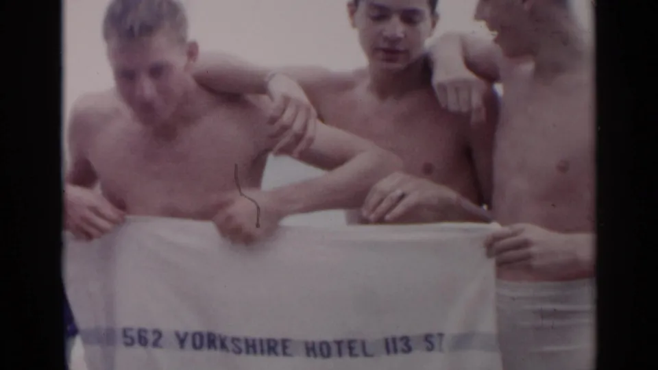 Three young men at a New York beach hold a white towel marked with Yorkshire Hotel and 113 St. text.