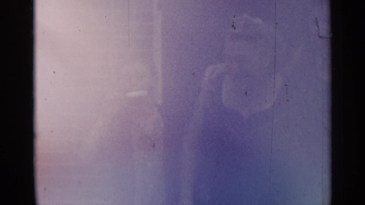 Soft, underexposed frame with faint figures behind blue-purple film haze.