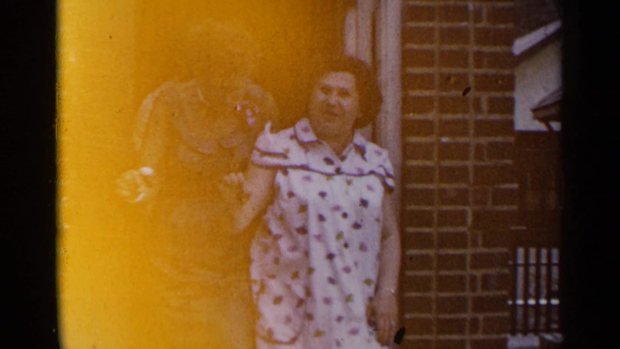 Woman in a polka-dot dress stands near another adult outside a brick building.