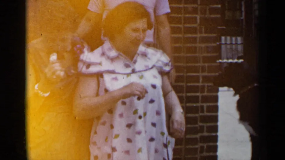 1954 New York frame of women smiling near the camera outside a brick building, with warm orange exposure across the image.