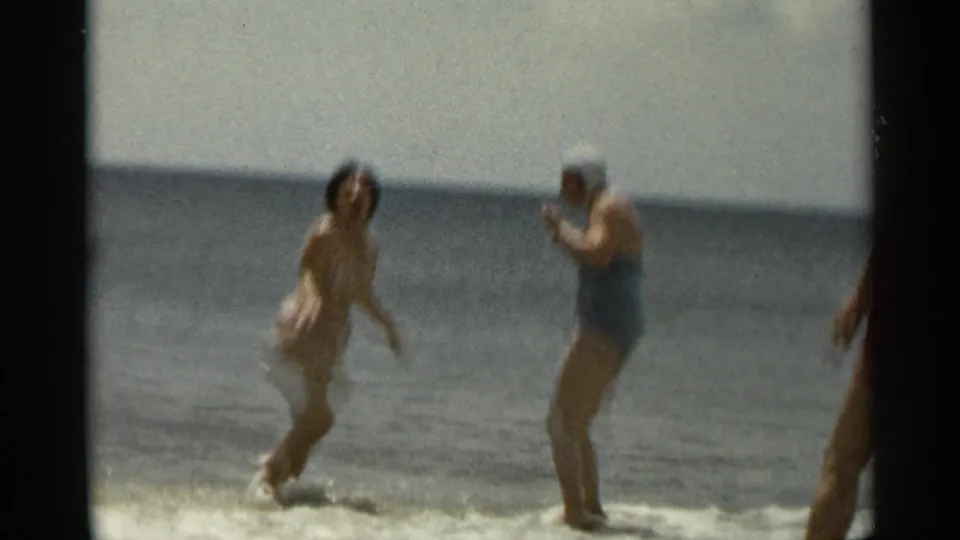 1954 New York 8mm beach frame of adult women reacting playfully in shallow ocean waves, with a partial figure at the right edge.