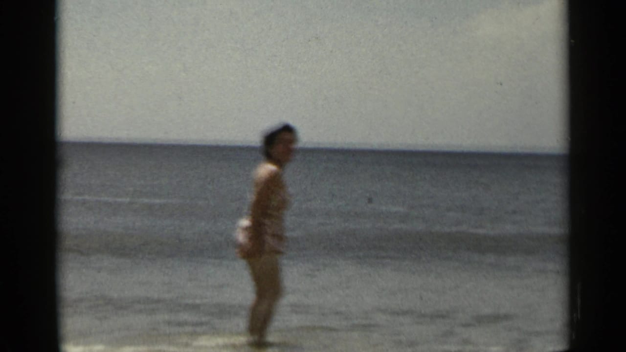 Woman in a swimsuit standing in shallow surf with the ocean horizon behind her.