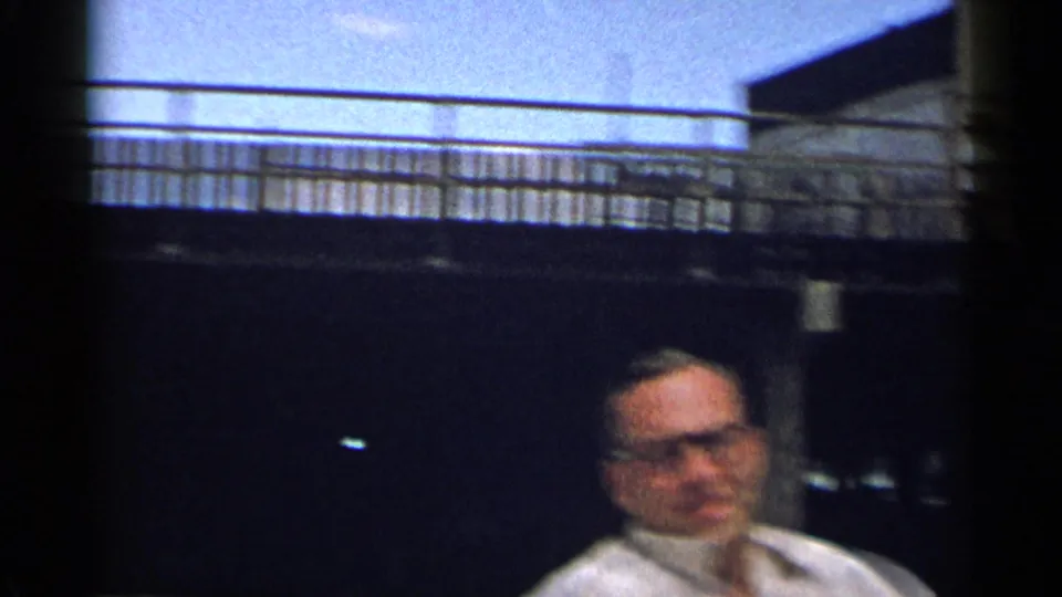 A softer frame shows the seated man in glasses beneath a railing, with the outdoor setting and bench partly visible.