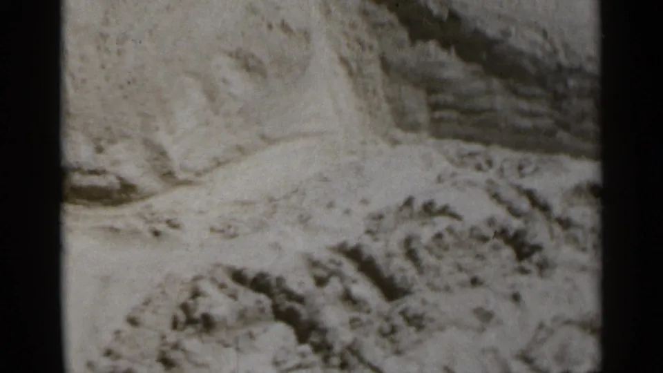 Close 8mm frame of textured beach sand, with a hand partly visible near the edge during the New York boardwalk outing.