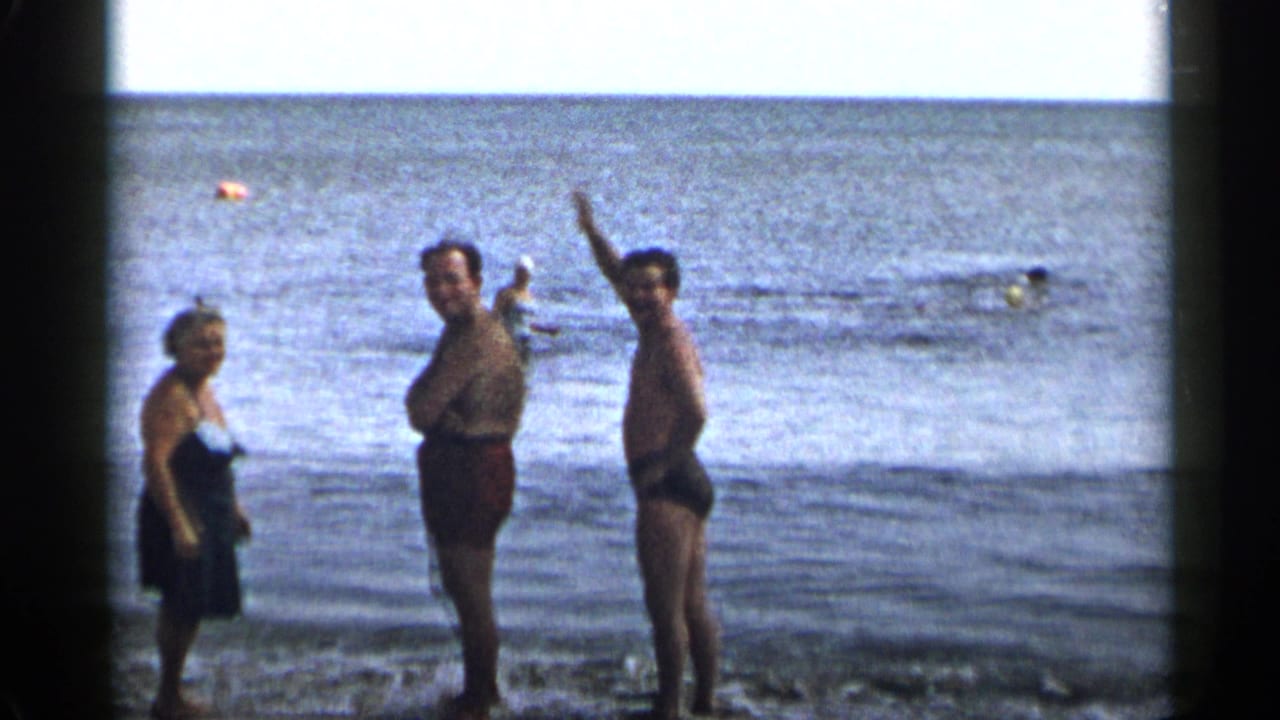 Three adults stand in shallow surf near the shoreline.