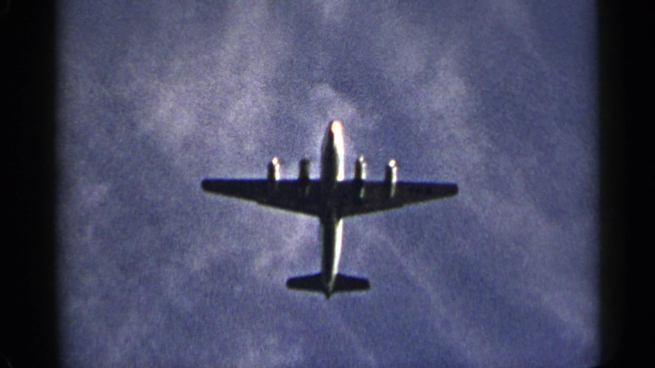 Propeller aircraft viewed from below with wings spread against mottled clouds.