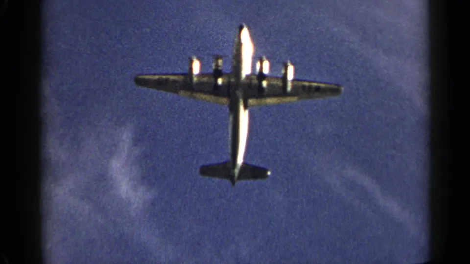 Close 8mm view of a large mid-century propeller aircraft passing overhead in New York, dated by metadata to 1954.