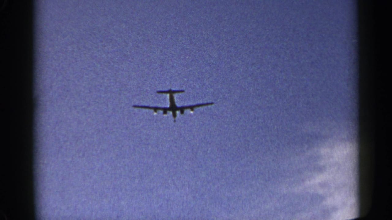 Airplane silhouette centered against blue sky with visible film gate edges.