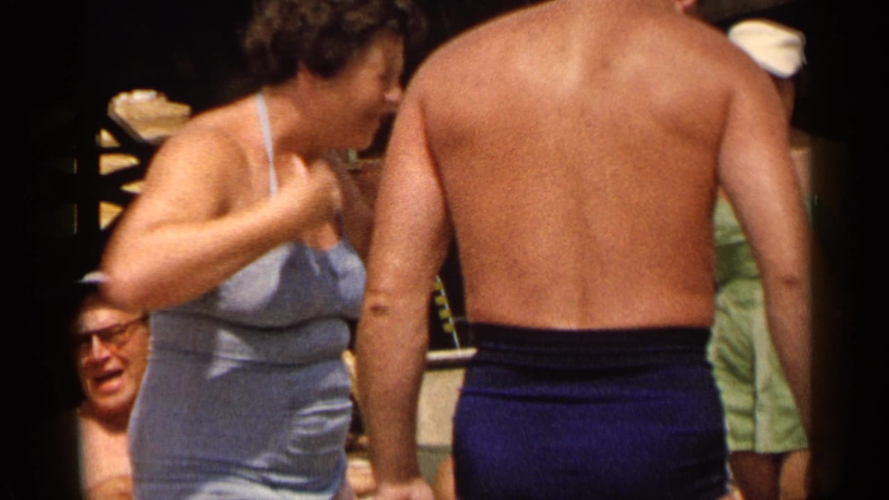 Woman in a light blue swimsuit stands near a shirtless man in blue bathing trunks.