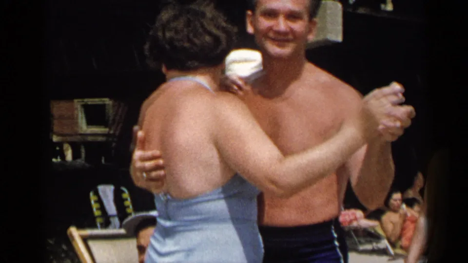 In 1954 New York home-movie footage, a shirtless man dances with a woman in a light blue swimsuit at a beach party.