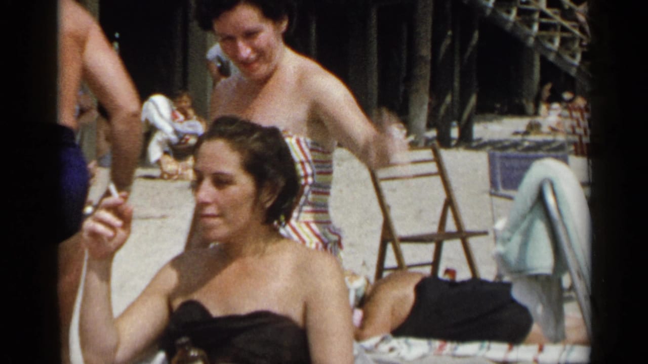 Woman in a black strapless top smokes while seated near other beach guests.