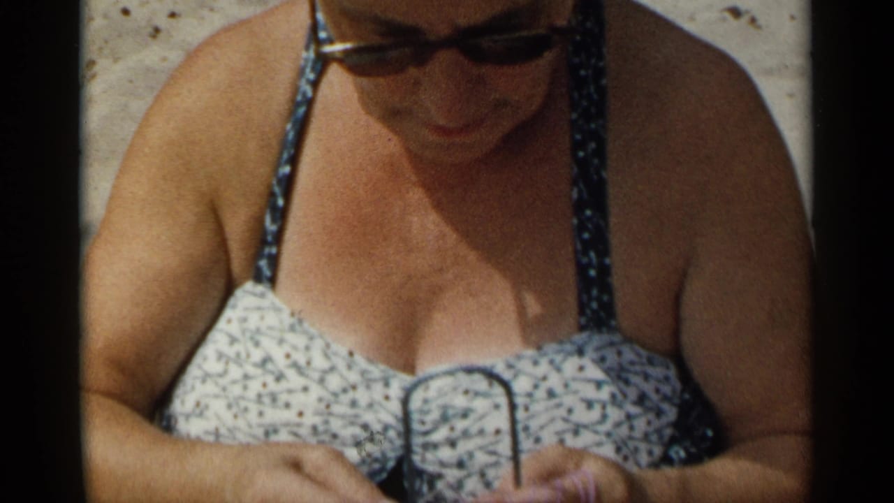 Woman in sunglasses and patterned swimsuit looking down at yarn and a small metal loom.
