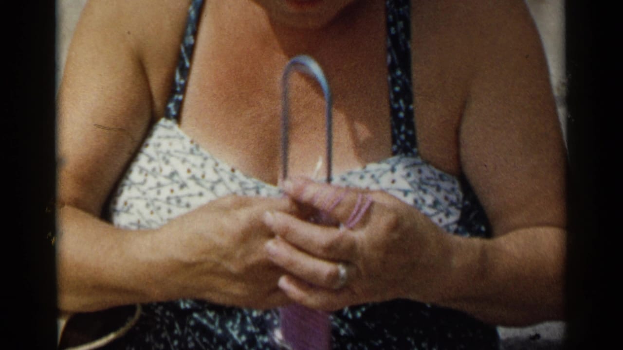 Close 1954 New York home-movie view of a woman in a patterned swimsuit holding a metal loom and purple yarn.