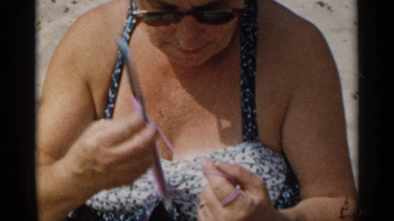 Woman wearing sunglasses knits with purple yarn while looking down.