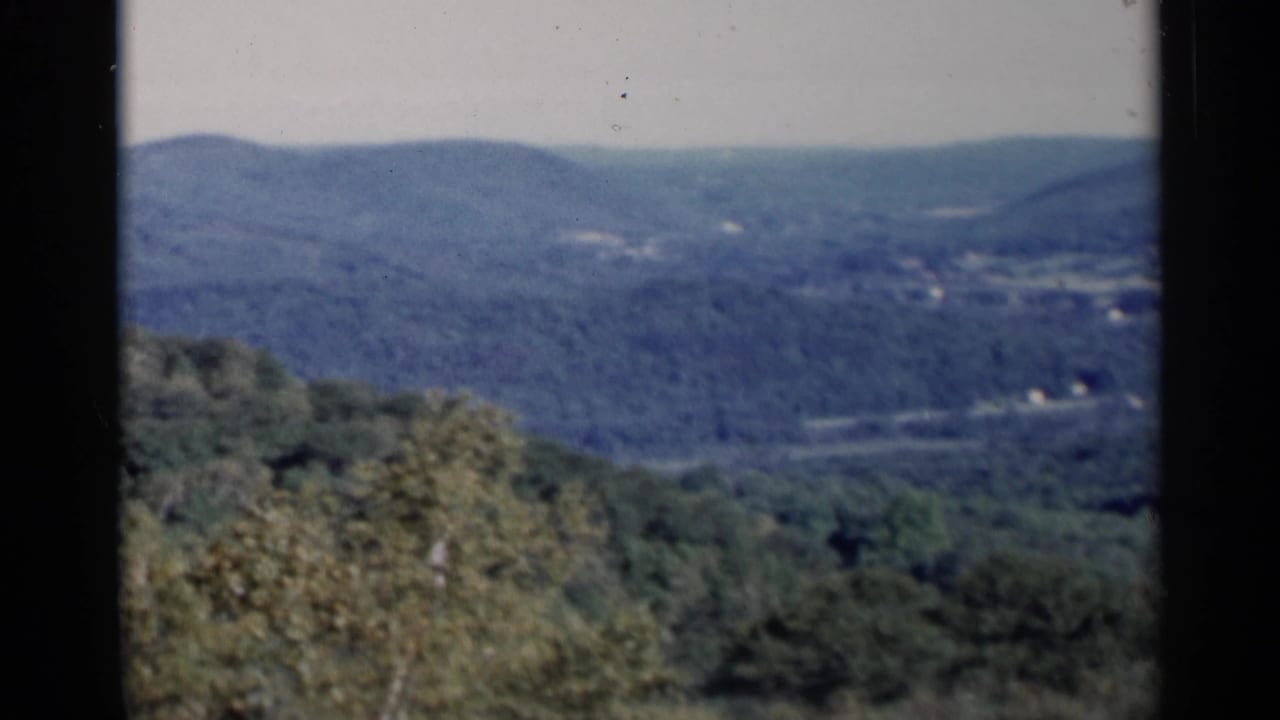 1955 Lake George home-movie view of wooded hills and hazy ridgelines seen from an elevated landscape vantage.
