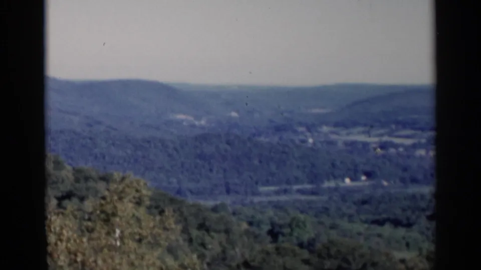 1955 Lake George scenic view across a wooded valley toward hazy blue hills, with 8mm borders visible.