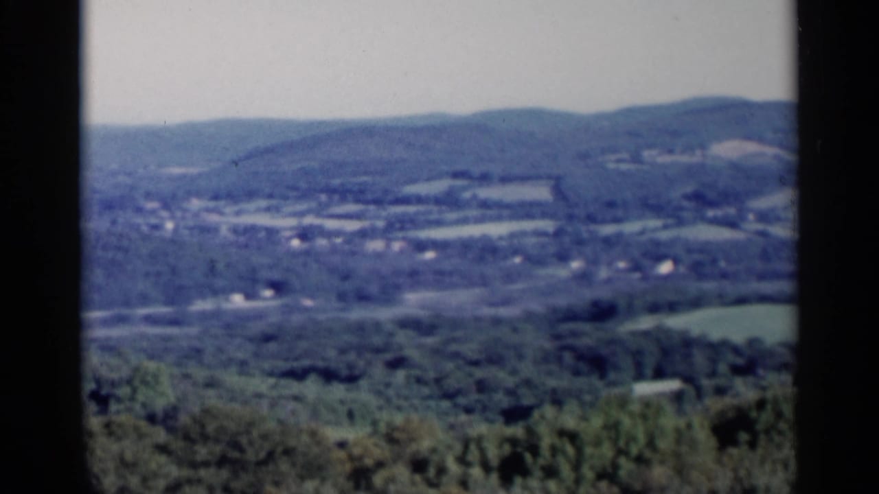 Rural valley with hills, fields, and dark film borders during a pan.