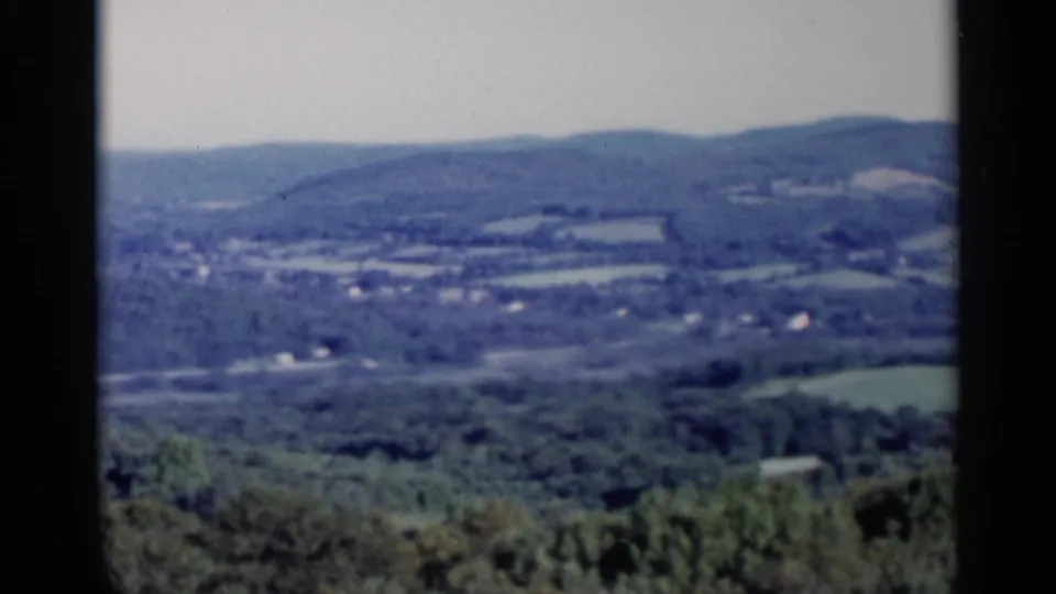 Lake George-area landscape frame with layered hills, patchwork fields, scattered buildings, and visible 8mm frame edges.