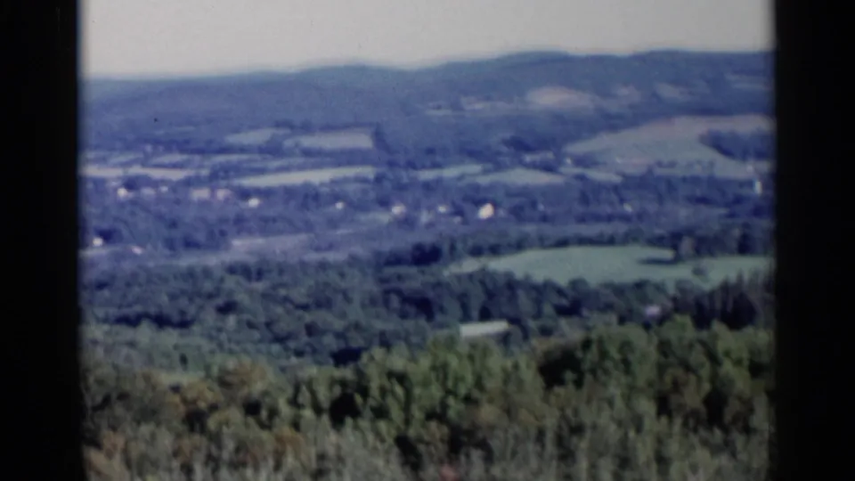 Mid-pan 1955 Lake George-area view with softened focus on fields, tree lines, hills, and distant rural buildings.