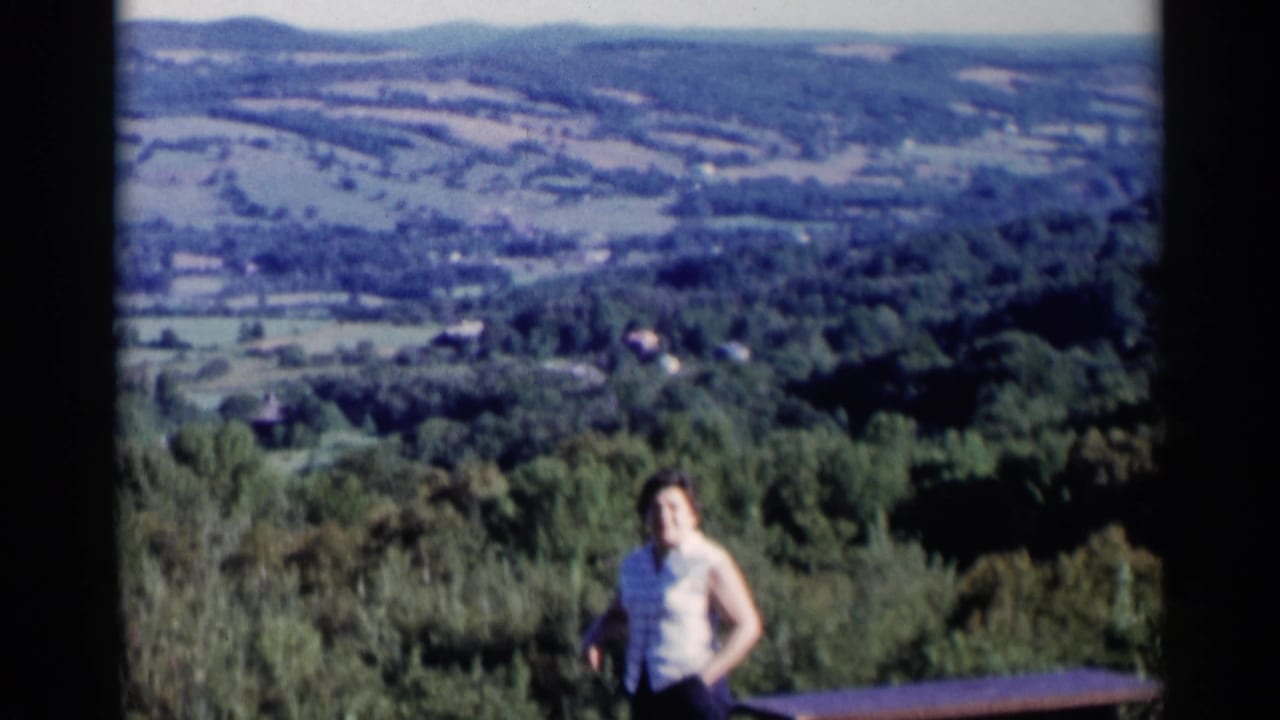 Woman standing before a wooded valley and distant hills.