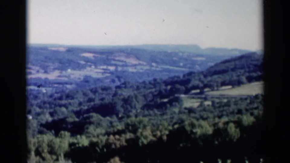 1955 Lake George home-movie frame with the person mostly out of view as the camera holds on the valley and surrounding hills.