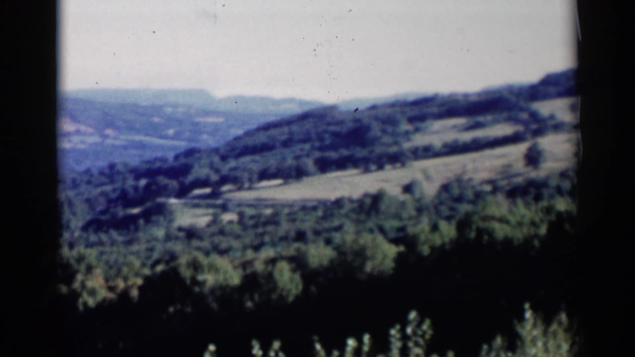 1955 Lake George-area home-movie view of rolling green hills, forested slopes, and pale sky from an elevated vantage.