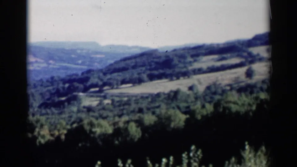 1955 Lake George-area home-movie view of rolling green hills, forested slopes, and pale sky from an elevated vantage.