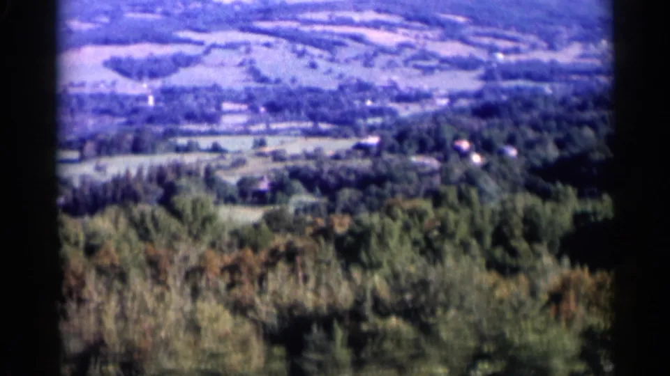 1950s 8mm view near Lake George showing wooded foreground, patchwork fields, and small distant houses.