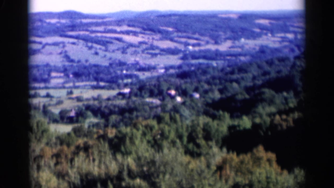 1955 Lake George, New York 8mm frame showing a soft elevated view across forests, patchwork fields, and rolling hills.