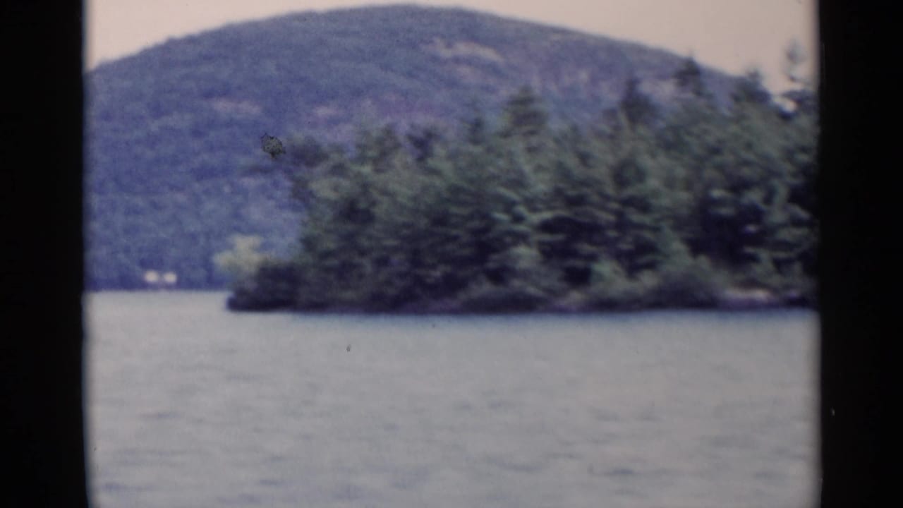Open lake view with wooded island at right and forested mountain beyond.