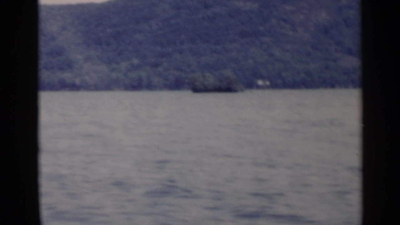 1955 Lake George home-movie frame showing rippled water and dark forested hills beyond the lake.