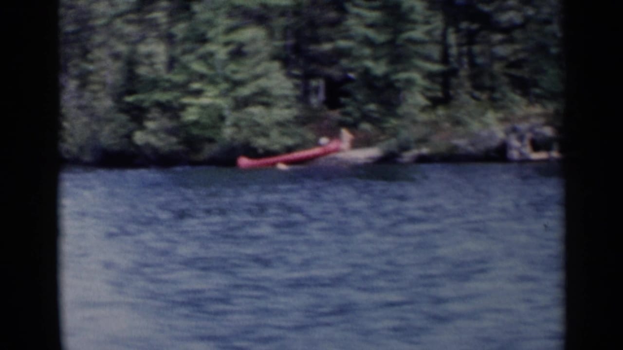 Red canoe near a forested lake shore with rippled water in the foreground.